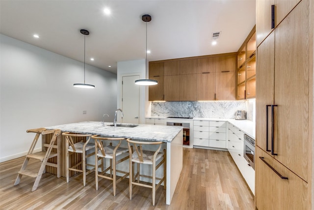 kitchen with stainless steel microwave, white cabinetry, sink, decorative backsplash, and hanging light fixtures