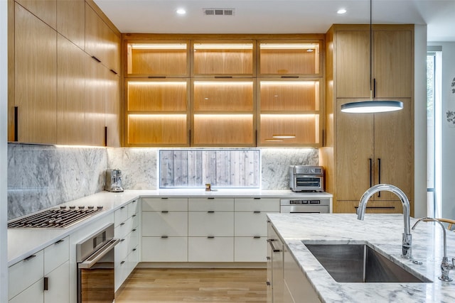 kitchen with sink, light stone counters, decorative light fixtures, oven, and white cabinets