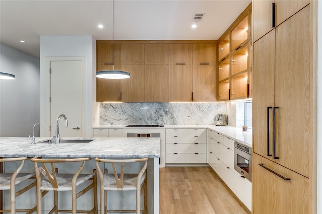 kitchen featuring stainless steel microwave, sink, a breakfast bar area, white cabinets, and light stone counters