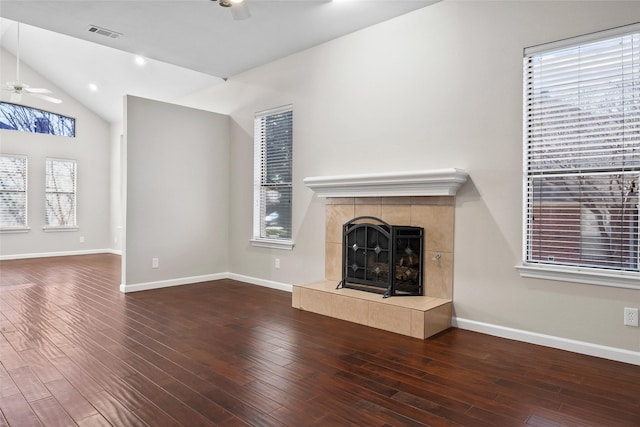 unfurnished living room featuring wood finished floors, a tiled fireplace, a wealth of natural light, visible vents, and ceiling fan