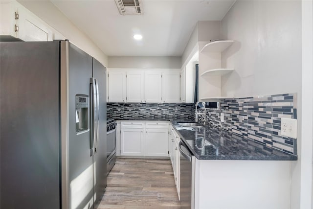 kitchen with appliances with stainless steel finishes, white cabinetry, sink, decorative backsplash, and dark stone counters