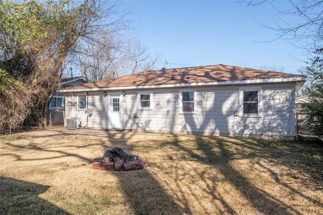 rear view of house with a lawn, central AC, and an outdoor fire pit