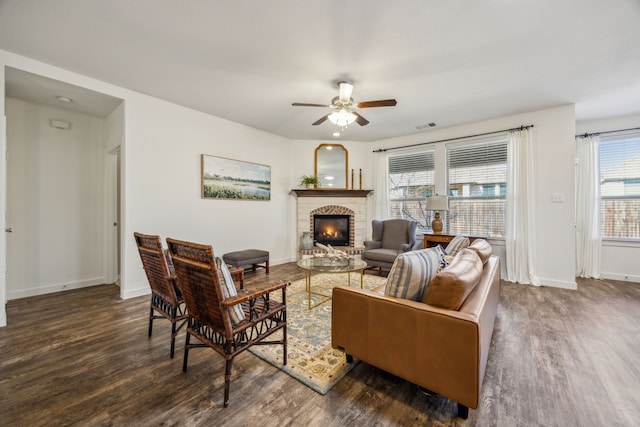 living room with a stone fireplace, dark wood-type flooring, and ceiling fan