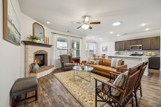 living room featuring ceiling fan, a stone fireplace, sink, and dark hardwood / wood-style flooring