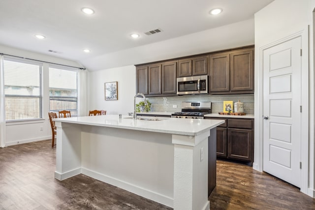 kitchen featuring tasteful backsplash, sink, stainless steel appliances, dark brown cabinets, and a center island with sink