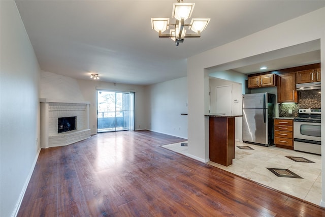 kitchen with tasteful backsplash, open floor plan, light wood-style flooring, under cabinet range hood, and appliances with stainless steel finishes