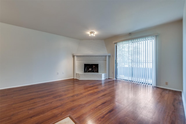 unfurnished living room with a brick fireplace and dark wood-type flooring