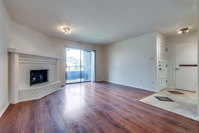unfurnished living room featuring wood finished floors, baseboards, and a brick fireplace