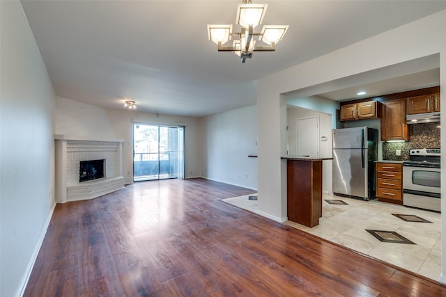 kitchen with a brick fireplace, appliances with stainless steel finishes, light wood-type flooring, and decorative backsplash