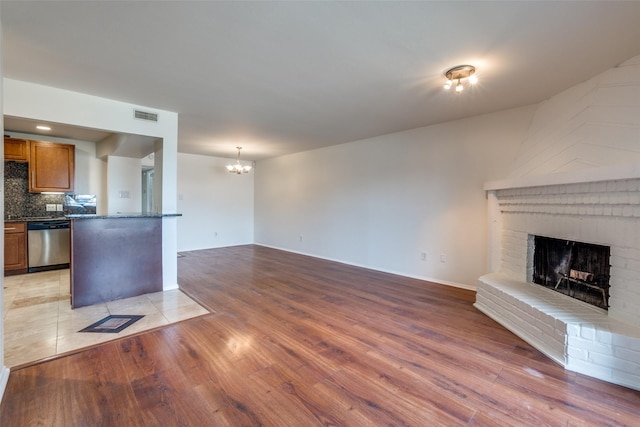 unfurnished living room featuring visible vents, baseboards, a brick fireplace, light wood-type flooring, and a chandelier
