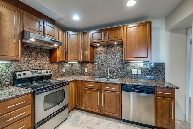 kitchen featuring dark stone counters, appliances with stainless steel finishes, under cabinet range hood, a sink, and brown cabinets