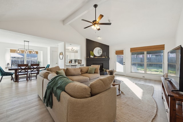 living room featuring ceiling fan, high vaulted ceiling, light hardwood / wood-style floors, a brick fireplace, and beamed ceiling