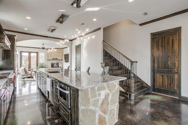 kitchen with sink, a breakfast bar, light stone countertops, decorative light fixtures, and a large island with sink