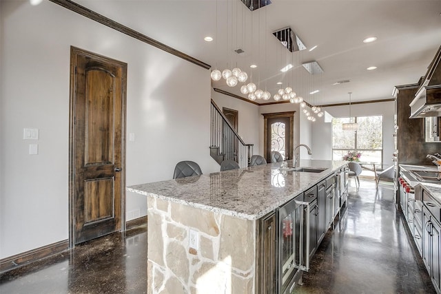 kitchen featuring a spacious island, sink, light stone counters, hanging light fixtures, and beverage cooler