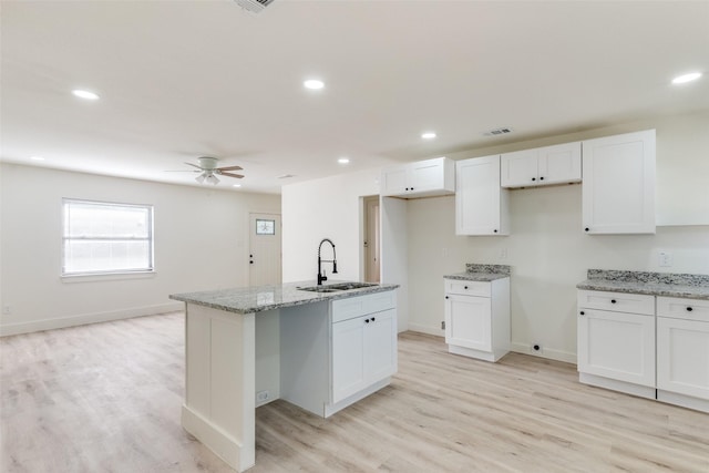 kitchen with sink, light stone counters, light wood-type flooring, an island with sink, and white cabinets