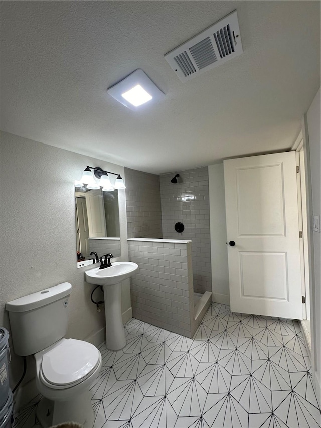 bathroom with tiled shower, sink, a textured ceiling, and toilet