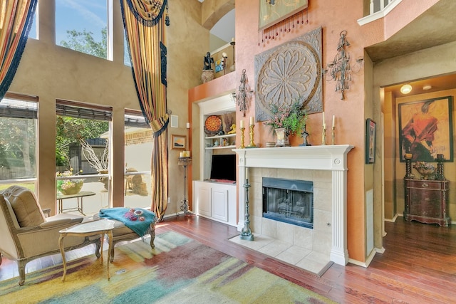 living area featuring a tiled fireplace, wood-type flooring, a towering ceiling, and built in features