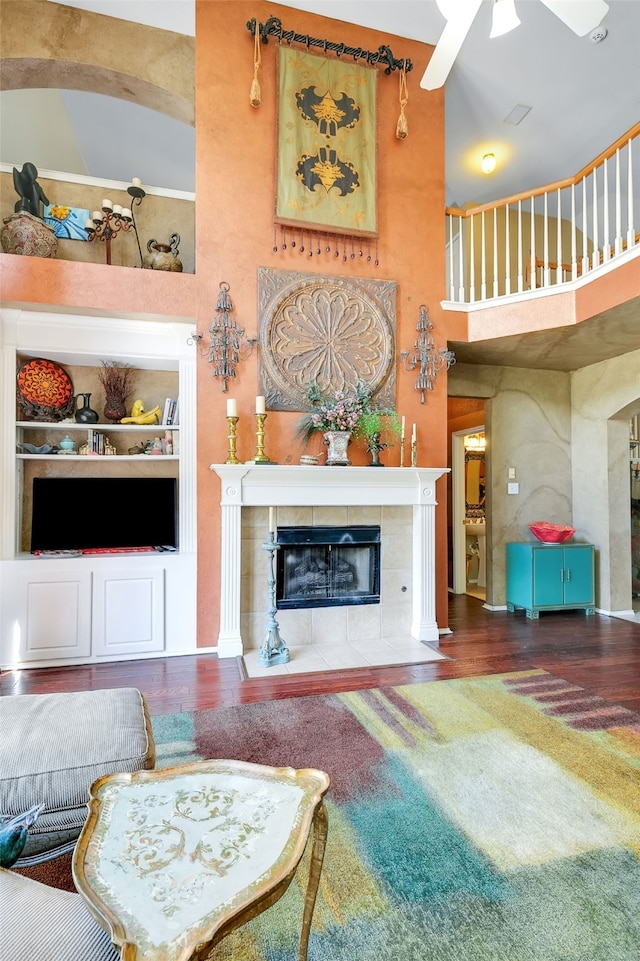 living room with hardwood / wood-style flooring, built in features, a tile fireplace, and a high ceiling