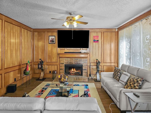 living room featuring wood walls, wood-type flooring, ceiling fan, a brick fireplace, and a textured ceiling