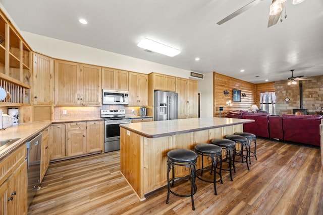 kitchen with a center island, a wood stove, a kitchen breakfast bar, stainless steel appliances, and hardwood / wood-style floors