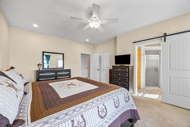 carpeted bedroom featuring a closet, a barn door, ceiling fan, and ensuite bathroom