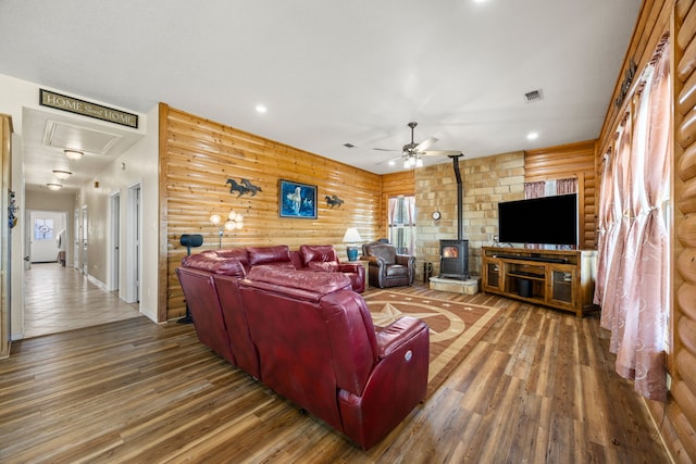 living room with wood-type flooring, a wood stove, a wealth of natural light, ceiling fan, and log walls