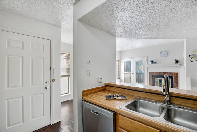 kitchen with sink, dishwasher, a textured ceiling, dark hardwood / wood-style flooring, and a brick fireplace