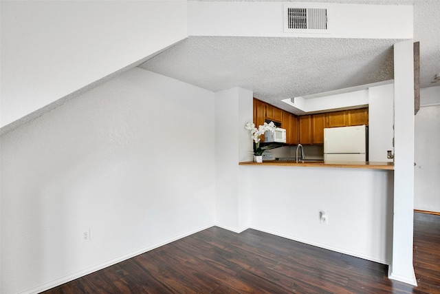 kitchen featuring dark wood-type flooring, white appliances, kitchen peninsula, and a textured ceiling