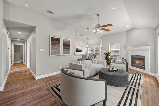 living room with a tile fireplace, vaulted ceiling, dark wood-type flooring, and ceiling fan