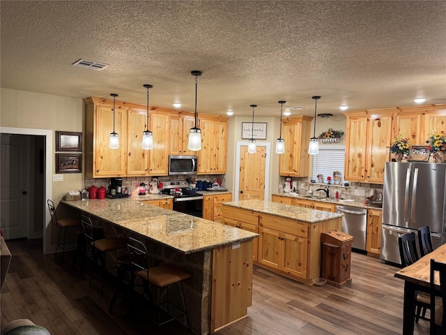 kitchen featuring stainless steel appliances, light stone counters, a kitchen bar, decorative light fixtures, and kitchen peninsula