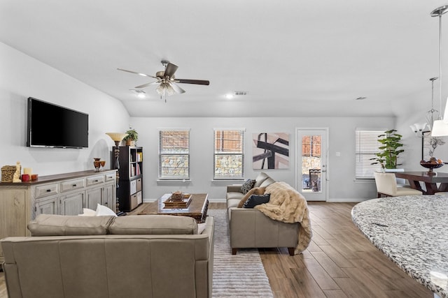 living room with ceiling fan with notable chandelier, vaulted ceiling, and light hardwood / wood-style floors