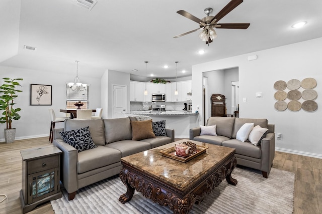 living room with ceiling fan with notable chandelier and light wood-type flooring