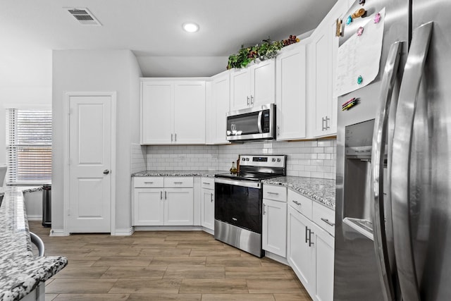 kitchen featuring stainless steel appliances, white cabinetry, light stone counters, and light hardwood / wood-style floors