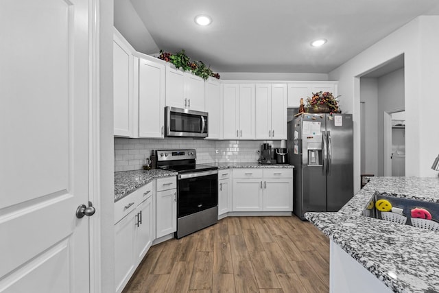 kitchen featuring light stone counters, wood-type flooring, appliances with stainless steel finishes, white cabinets, and backsplash