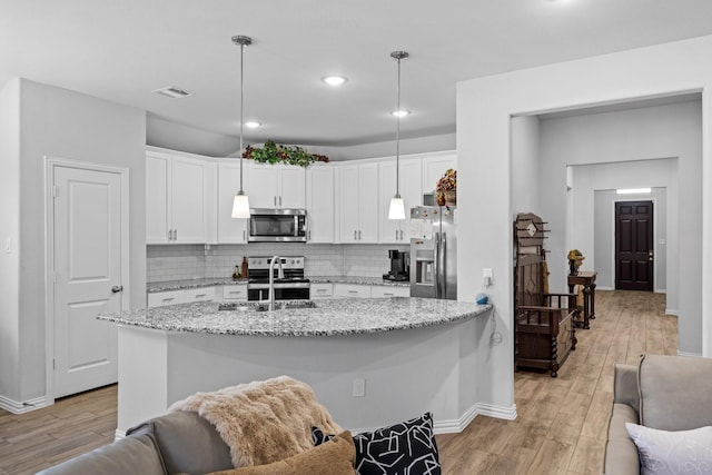 kitchen with sink, decorative light fixtures, appliances with stainless steel finishes, a kitchen island with sink, and white cabinets