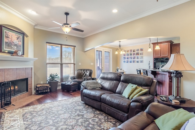 living room with ornamental molding, ceiling fan with notable chandelier, dark wood-type flooring, and a tile fireplace