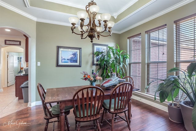 dining room featuring dark wood-type flooring, ornamental molding, a raised ceiling, and a chandelier