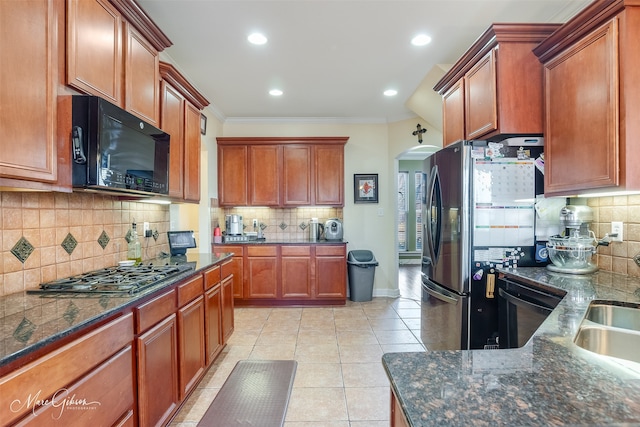 kitchen with light tile patterned flooring, appliances with stainless steel finishes, dark stone countertops, backsplash, and ornamental molding