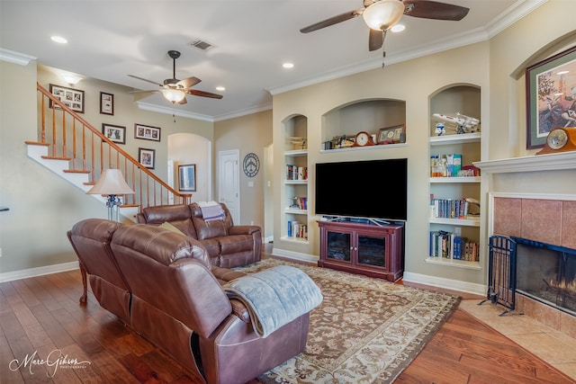 living room featuring built in shelves, crown molding, a tiled fireplace, and hardwood / wood-style floors