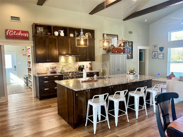 kitchen with beamed ceiling, a kitchen bar, a kitchen island with sink, high end stainless steel range, and light hardwood / wood-style floors