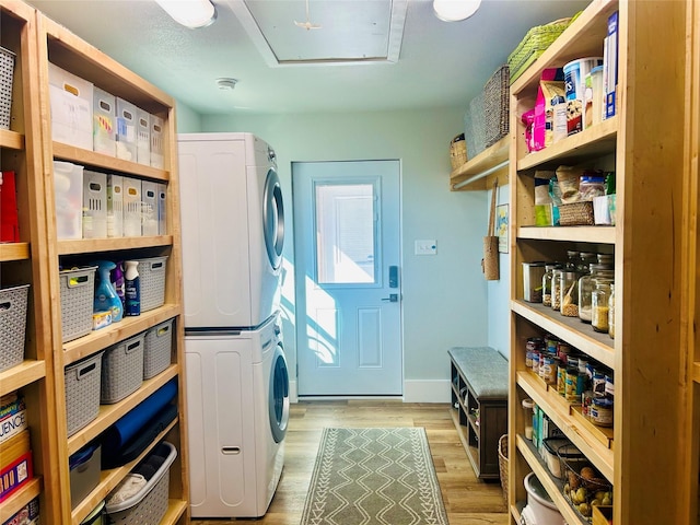 laundry area featuring light wood-type flooring, stacked washer and clothes dryer, baseboards, and laundry area