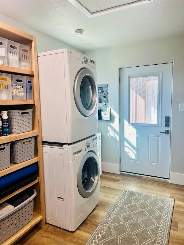 clothes washing area with stacked washer and clothes dryer, light wood-style flooring, a textured ceiling, laundry area, and baseboards