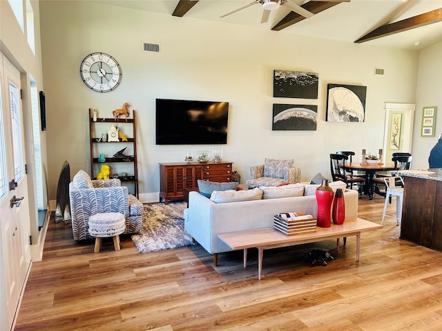 living area with a high ceiling, light wood-type flooring, beam ceiling, and a ceiling fan