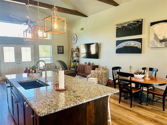 kitchen with sink, light hardwood / wood-style flooring, hanging light fixtures, a center island with sink, and french doors