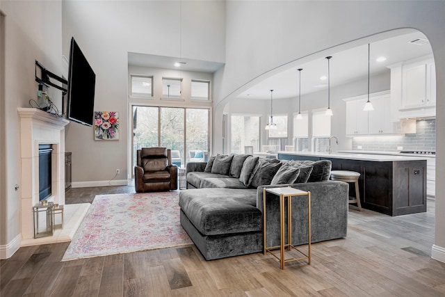 living room with a towering ceiling, a tiled fireplace, sink, and light wood-type flooring