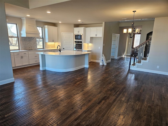 kitchen featuring built in microwave, an island with sink, white cabinetry, oven, and custom exhaust hood