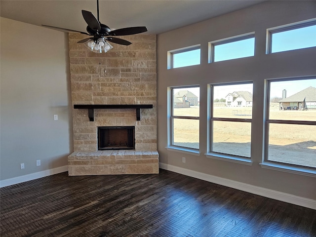 unfurnished living room featuring hardwood / wood-style flooring, ceiling fan, and a stone fireplace