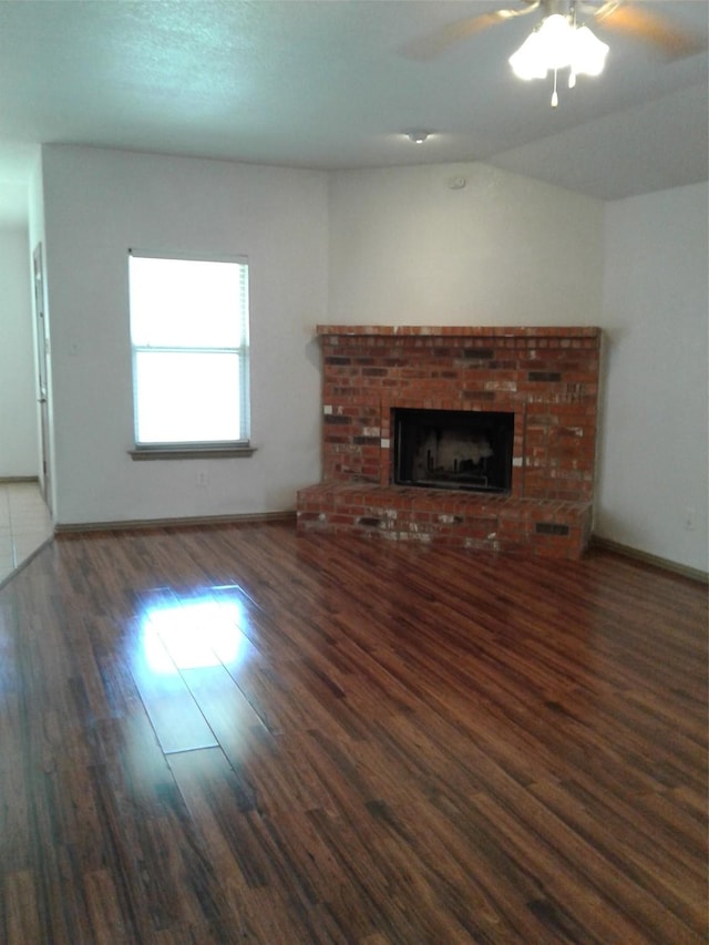 unfurnished living room featuring a brick fireplace, dark wood-type flooring, and ceiling fan