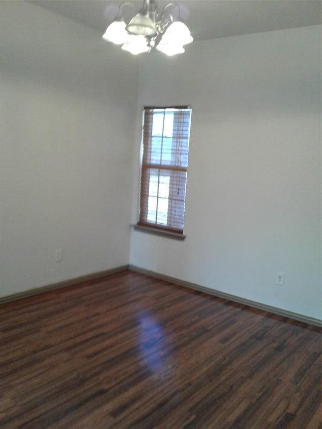 empty room with dark wood-type flooring and a notable chandelier