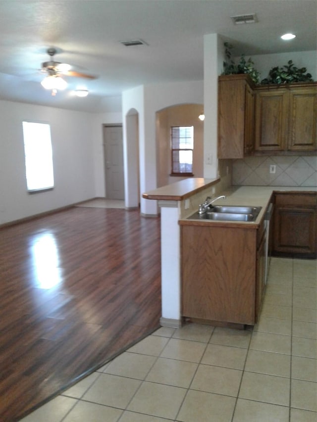 kitchen featuring light tile patterned flooring, sink, decorative backsplash, ceiling fan, and kitchen peninsula